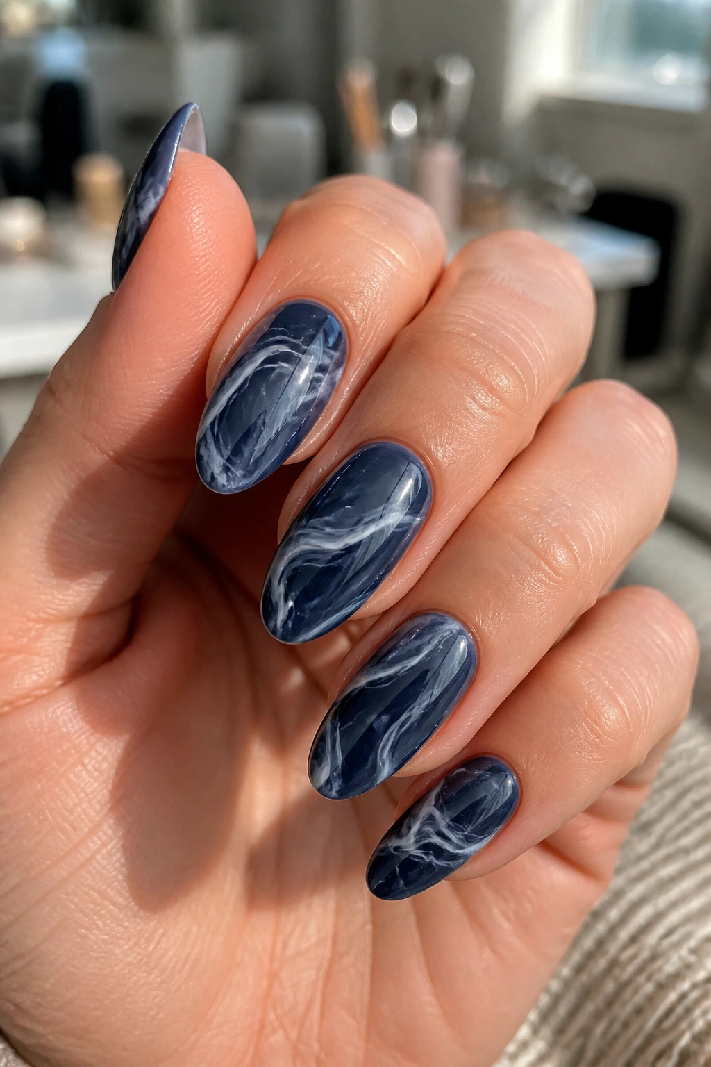 Close-up of almond nails with navy swirl art and milky white lines in a sunlit nail salon