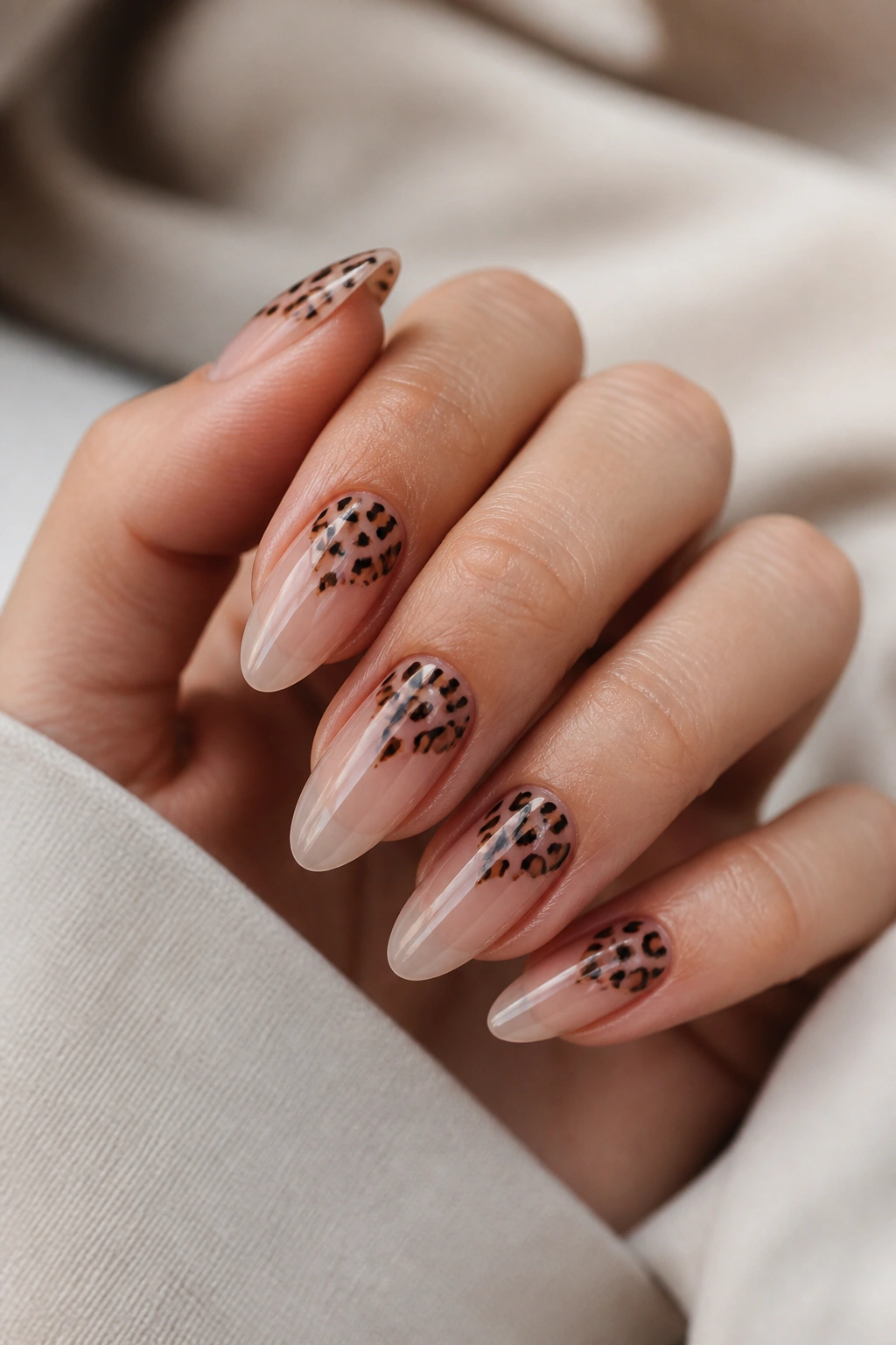 Close-up of clear almond nails with scattered cheetah spots and open space