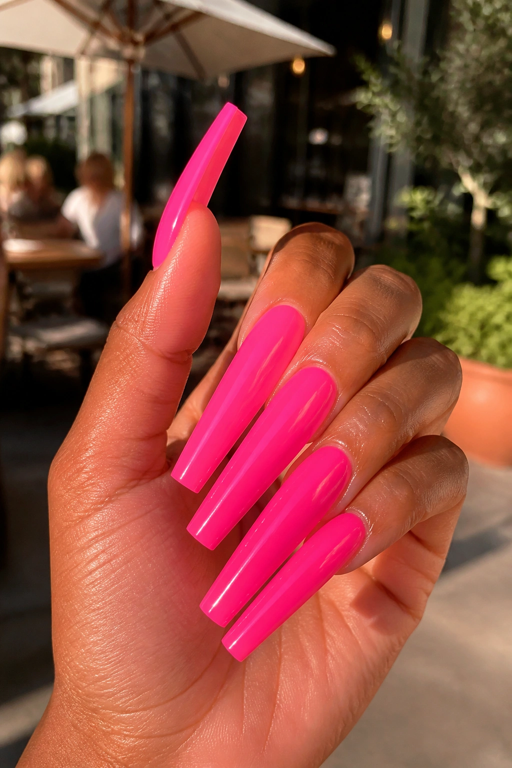 Close-up of neon hot pink extra-long coffin nails outdoors