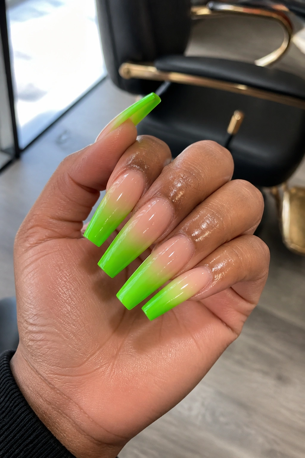Close-up of long coffin nails with neon green ombré fade in a salon setting