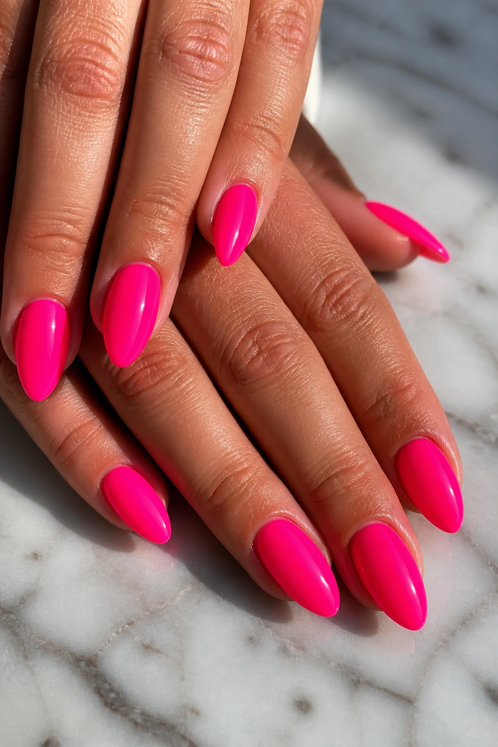 Close-up of solid neon hot pink almond nails on a real hand with glossy finish