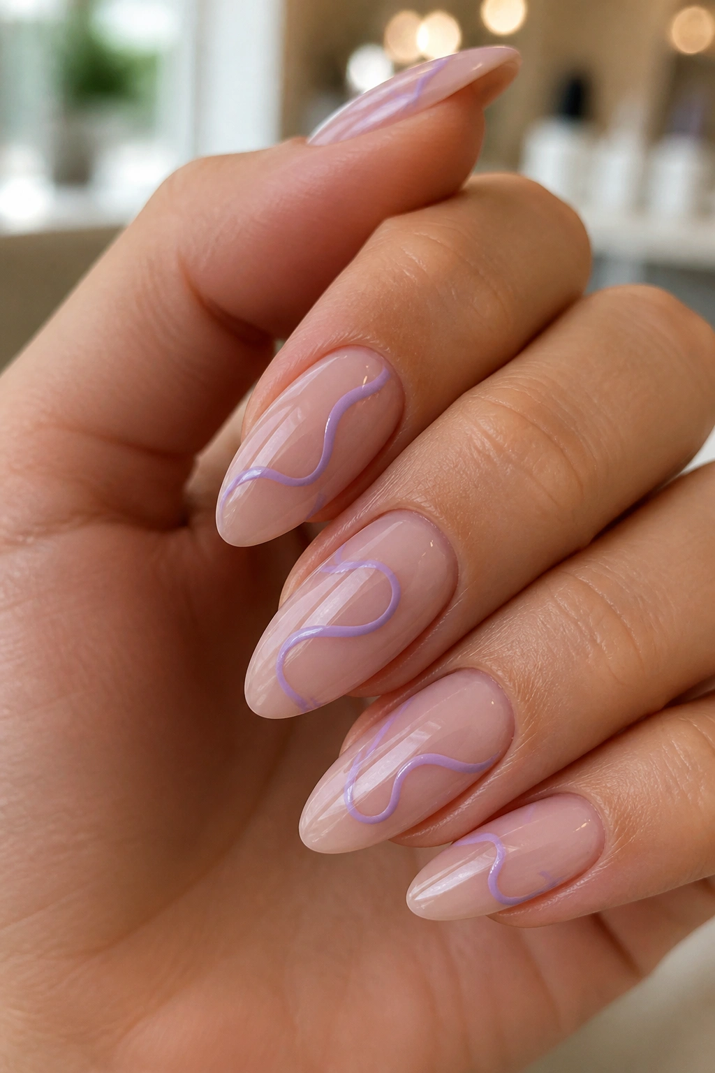 Close-up of a hand showing nude almond nails with abstract lavender line art.