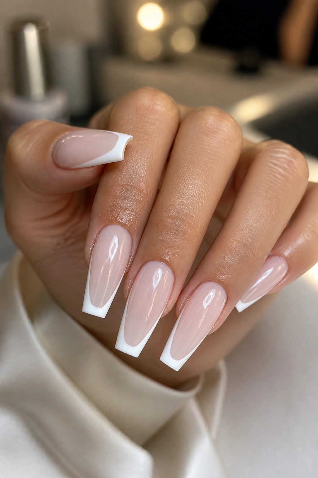 Close-up of hands displaying nude base with white tips and glossy finish on coffin nails.