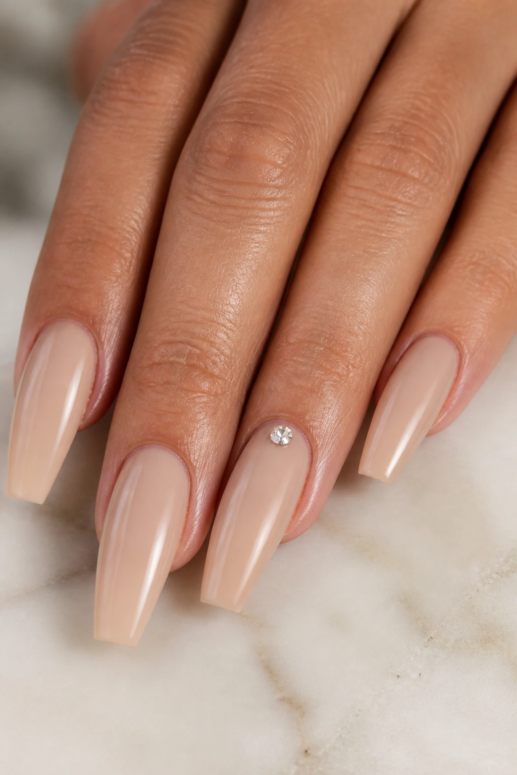 Close-up of nude beige coffin nails with a single crystal at the cuticle