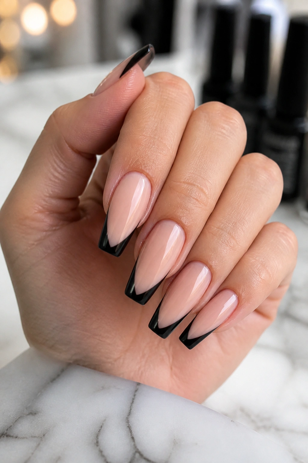 Close-up of nude coffin nails with black V-tips on a manicured hand