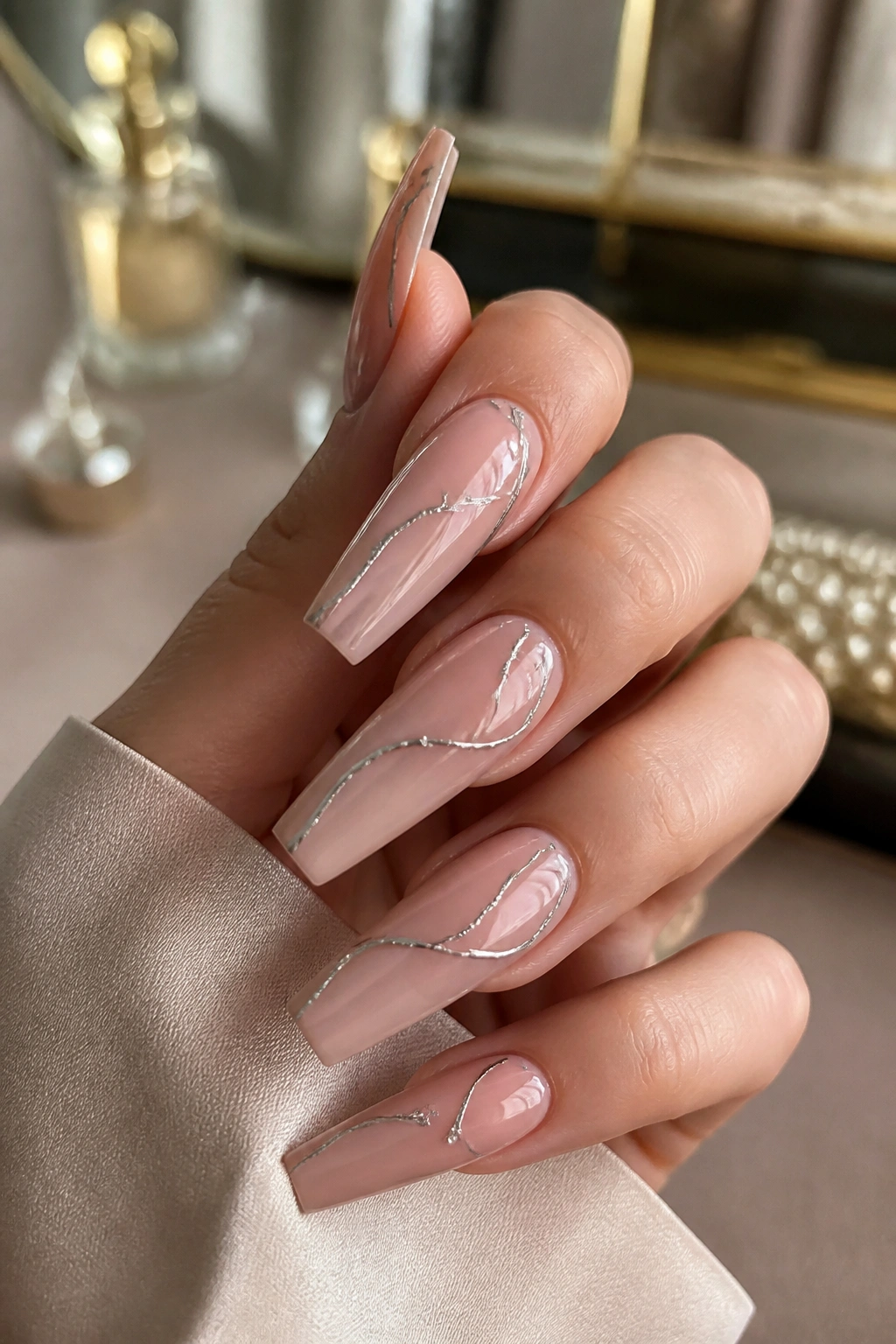 Close-up of nude lip-gloss nails with fine silver swirls.