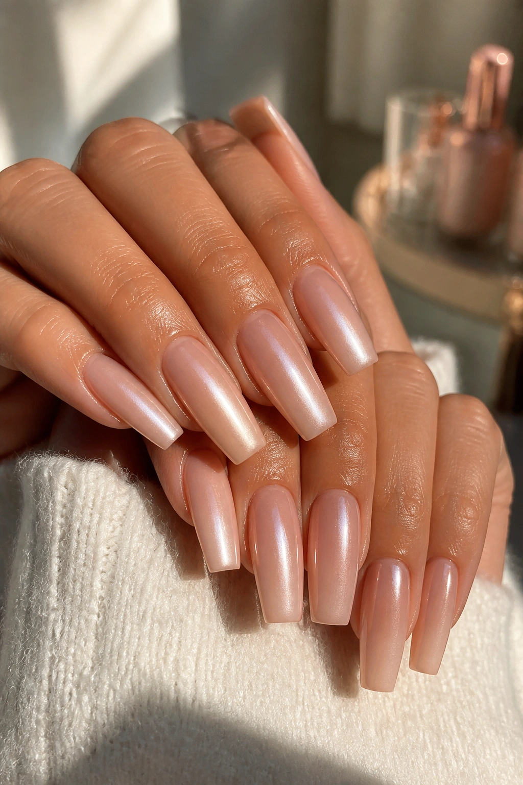 Close-up of hands showing glazed nude pearl coffin nails with pink-beige undertones.