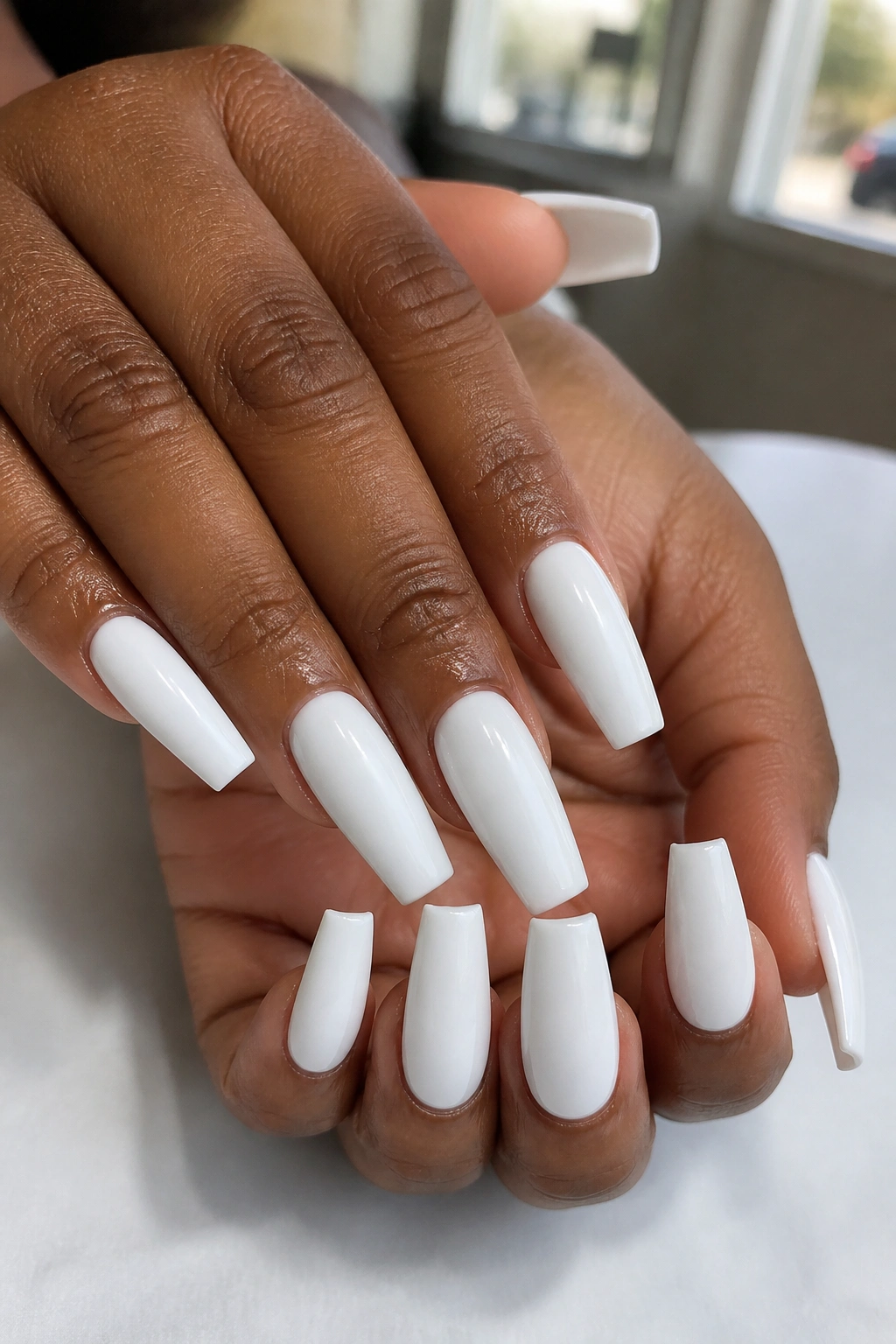 Close-up of real hands with opaque white coffin nails and a glossy finish.