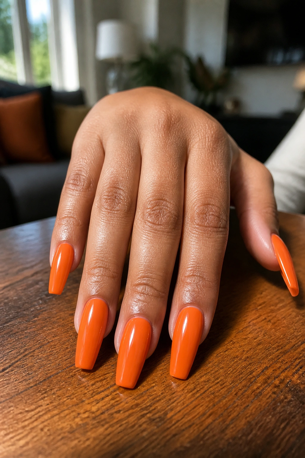 Close-up of a real woman's hand showing orange coffin nails on a wooden surface