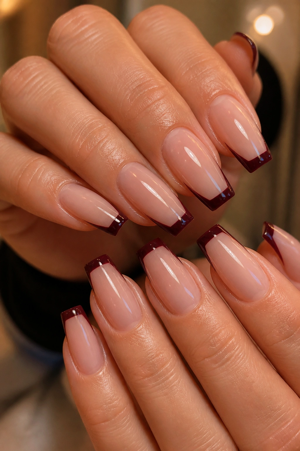 Close-up of glossy oxblood micro French tip coffin nails on a sheer nude base