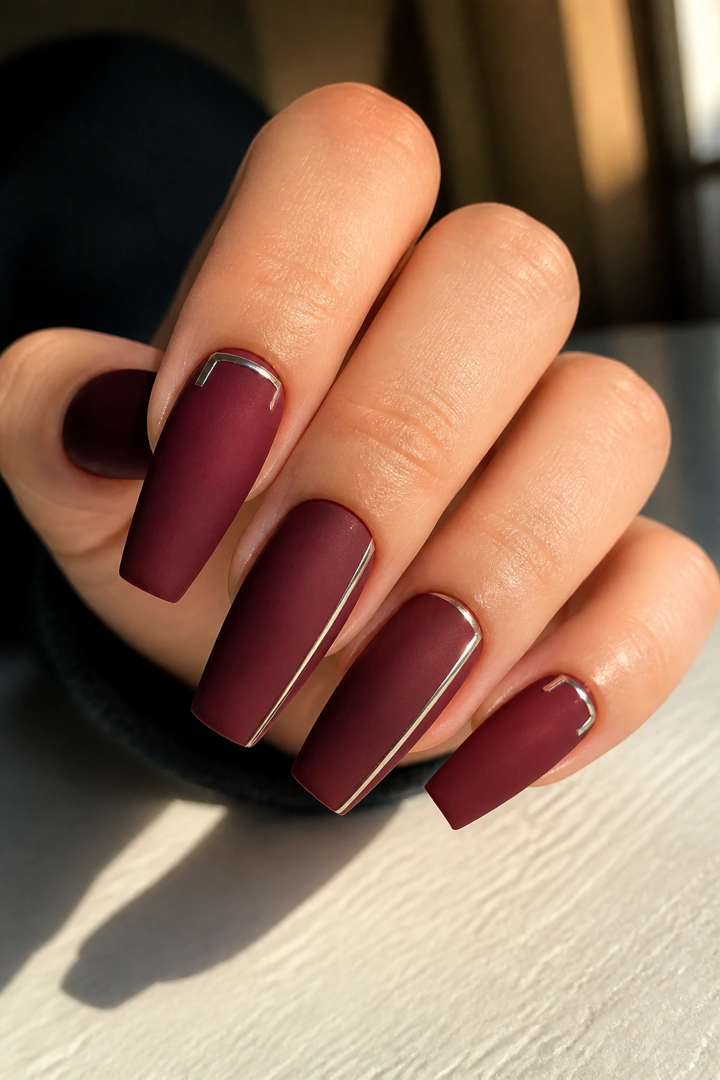 Close-up of oxblood matte coffin nails with slim chrome detail on real hand