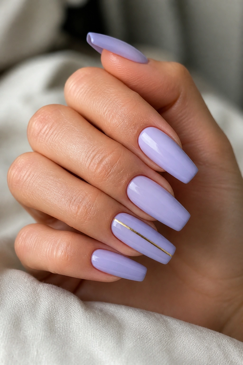 Close-up of pale lavender nails with a single gold stripe on accent nails