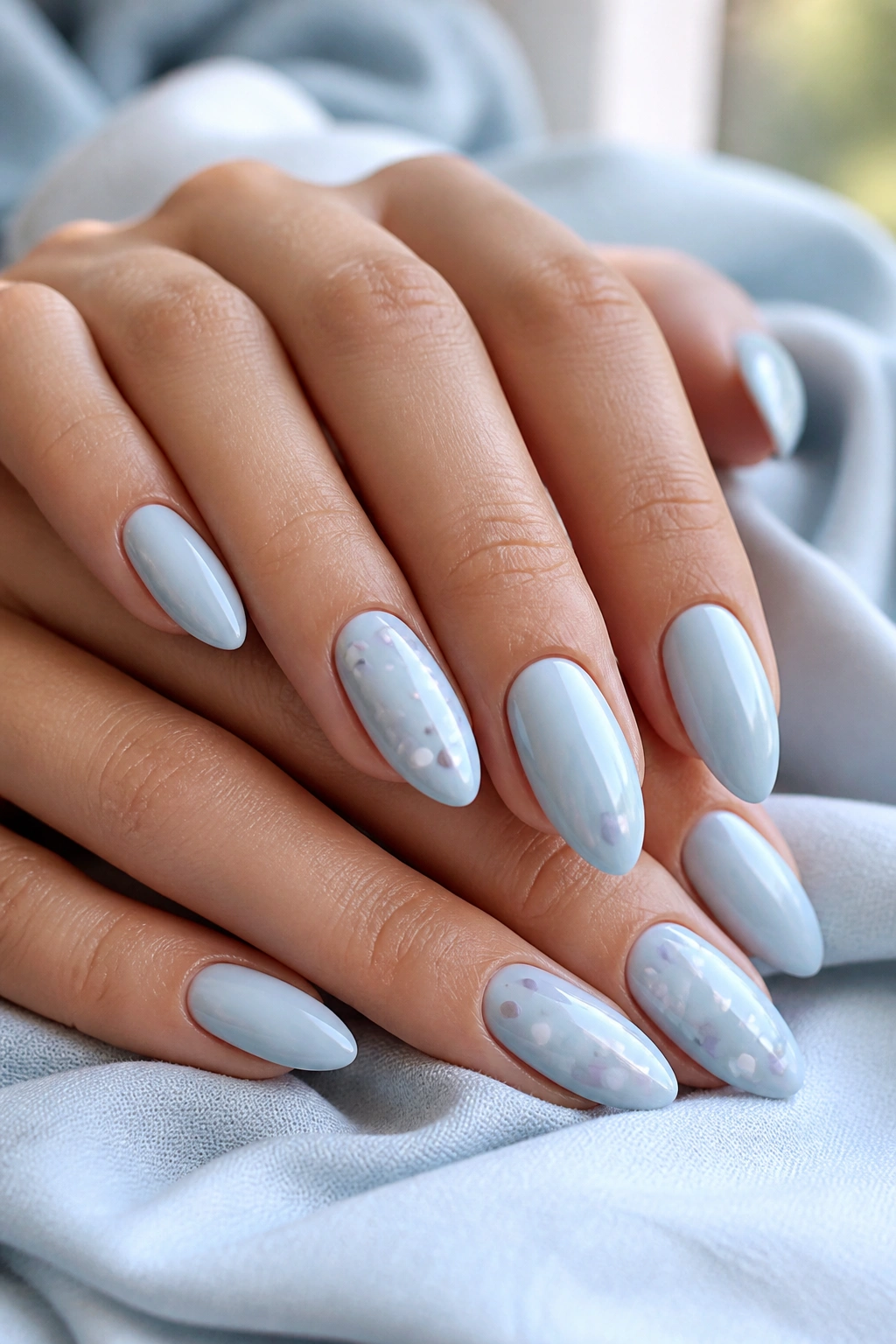 Close-up of pastel blue almond nails with sparse confetti dots on real hands