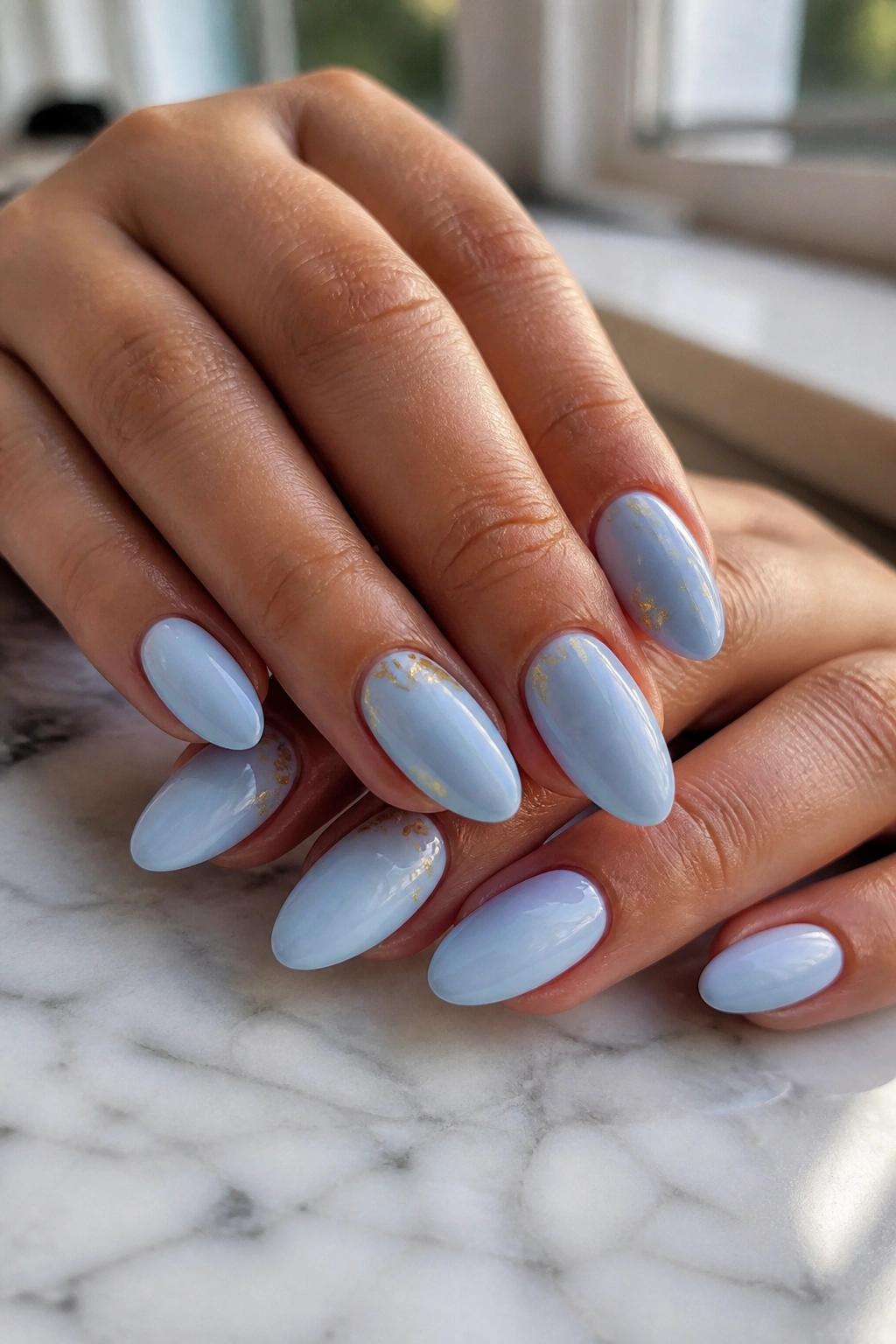 Close-up of pastel blue almond nails with gold foil flecks on real hands