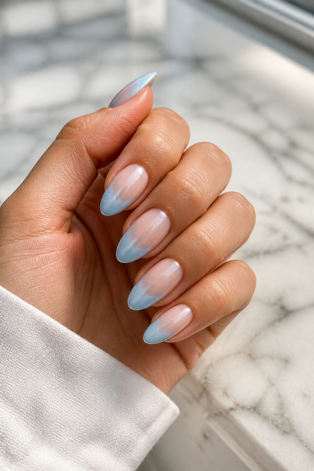 Close-up of pearl blue French ombré almond nails on a hand with nude-to-blue gradient