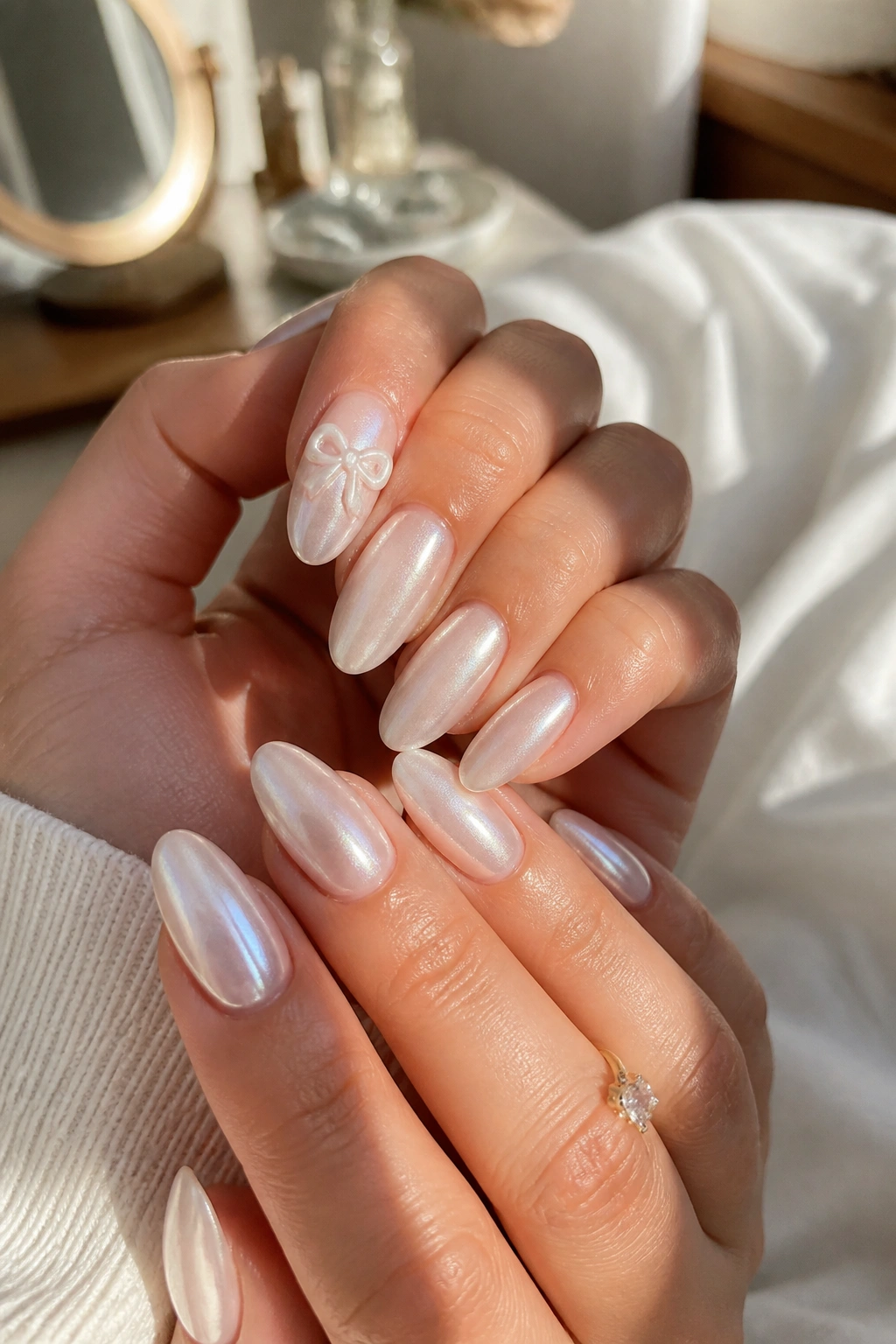 Close-up of pearl-finish almond nails with a soft carved bow on the index finger