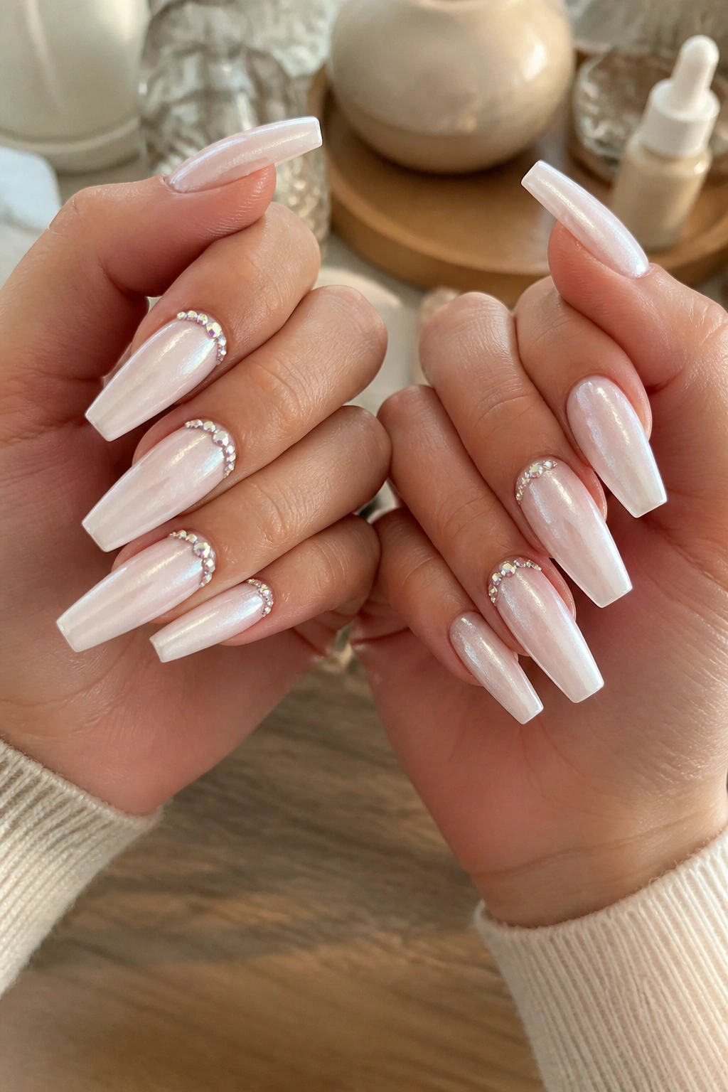 Close-up of hands with pearl coffin nails featuring a precise arc of crystals at the cuticle.