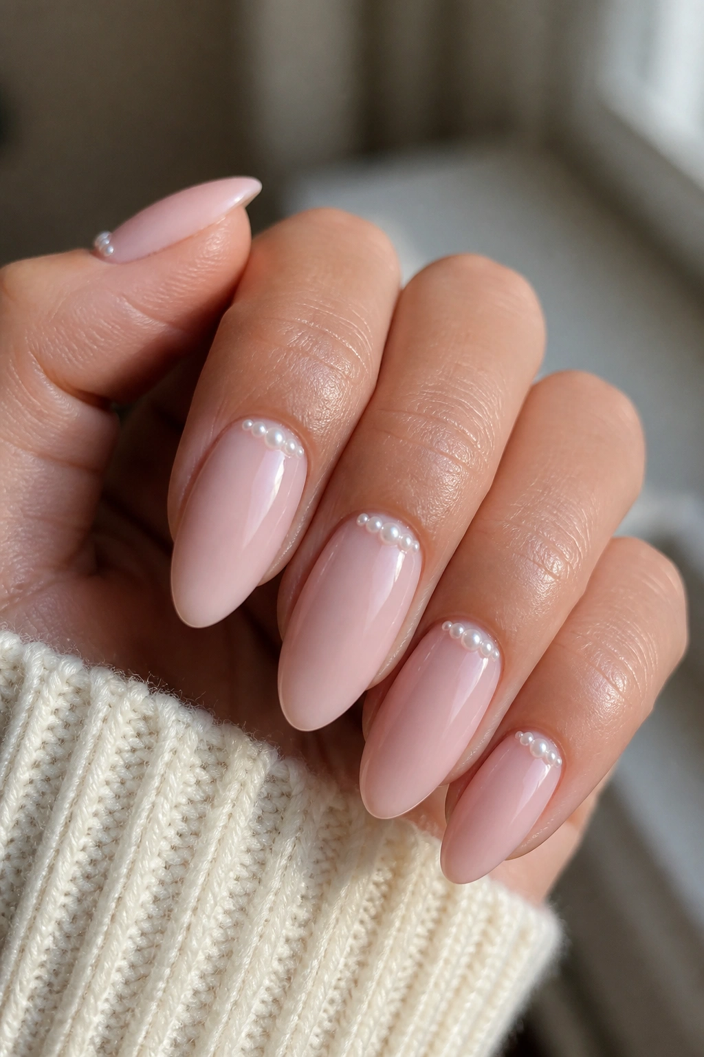 Close-up of tiny curved pearls along the cuticle on almond nails with a soft pink base