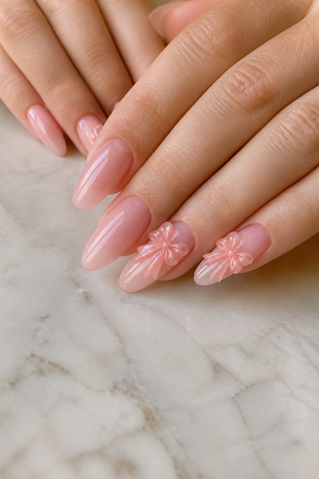 Close-up of sheer pink almond nails with raised 3D bows on accent nails