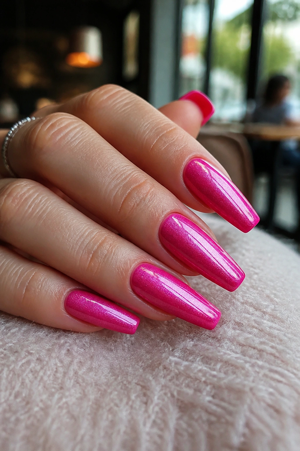 Close-up of real hand showing hot pink cat-eye coffin nails with a central magnetic stripe and star-dust shimmer