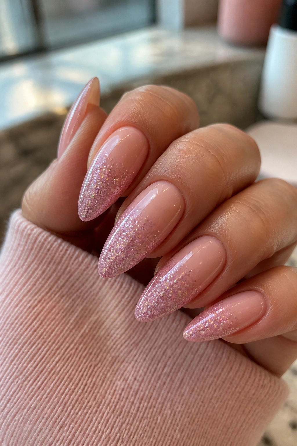 Close-up of long almond nails with pink glitter gradient