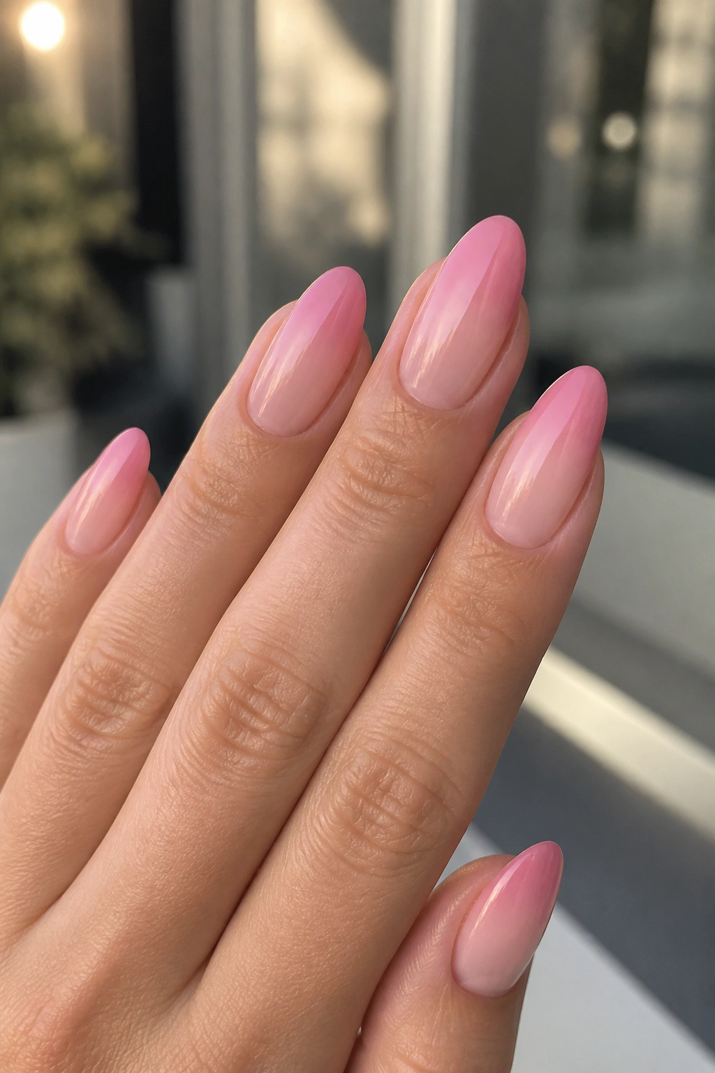 Close-up of a real hand with pink ombre almond nails fading from cuticle to tip