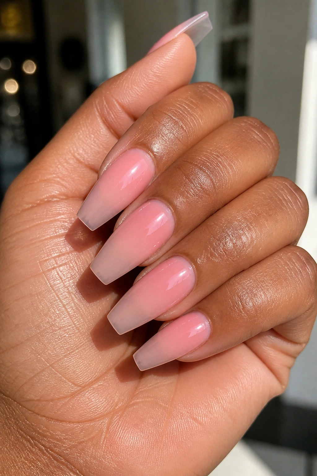 Close-up of pink ombre coffin nails on real hand in a warm salon setting