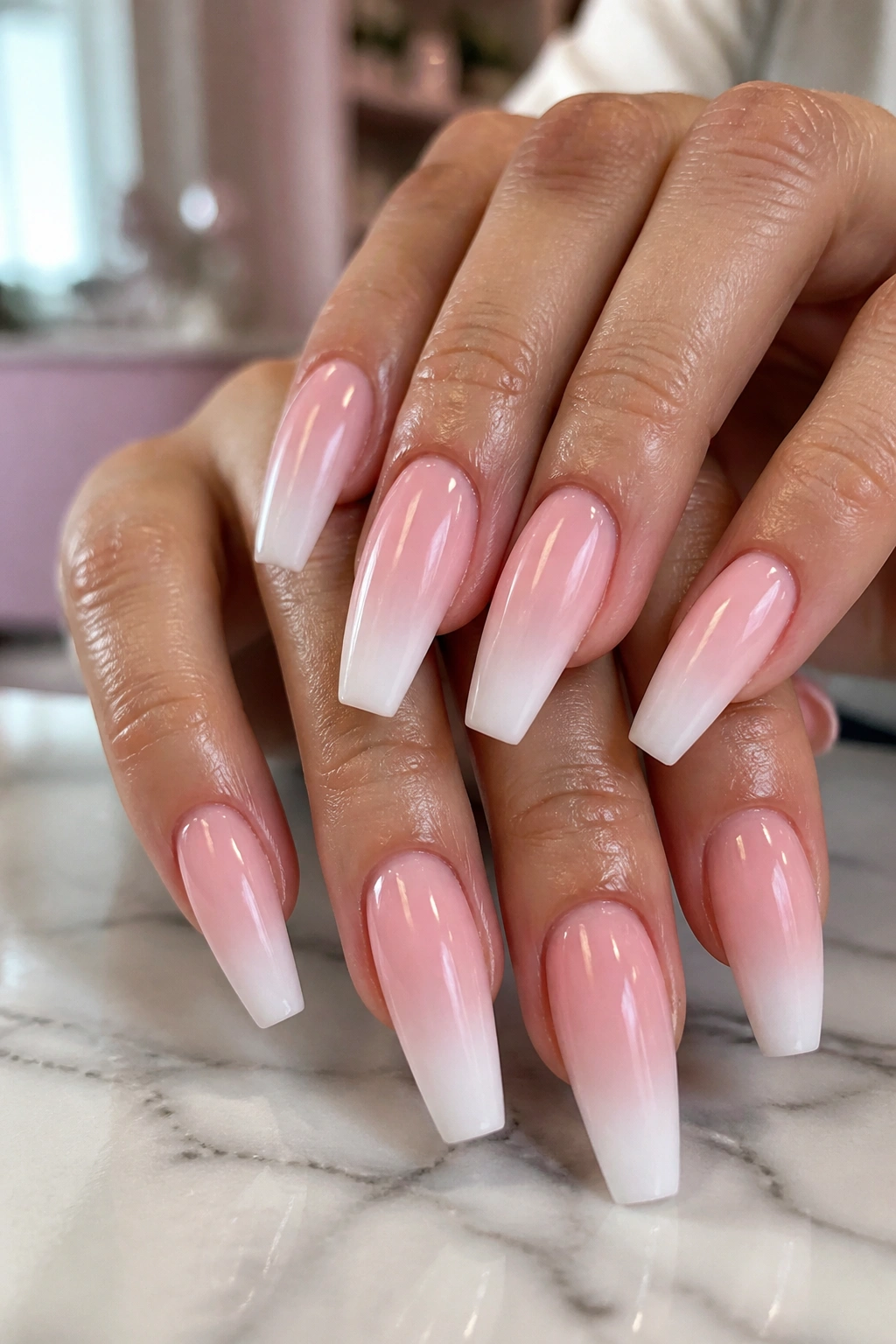 Close-up of baby pink to milky white ombre coffin nails on a real hand in a sunlit nail salon