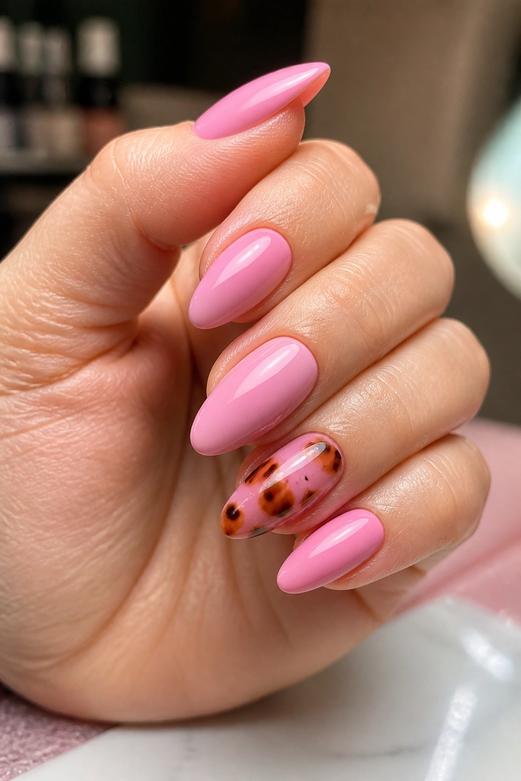 Close-up of pink almond nails with tortoiseshell accent on one or two nails in a glossy finish