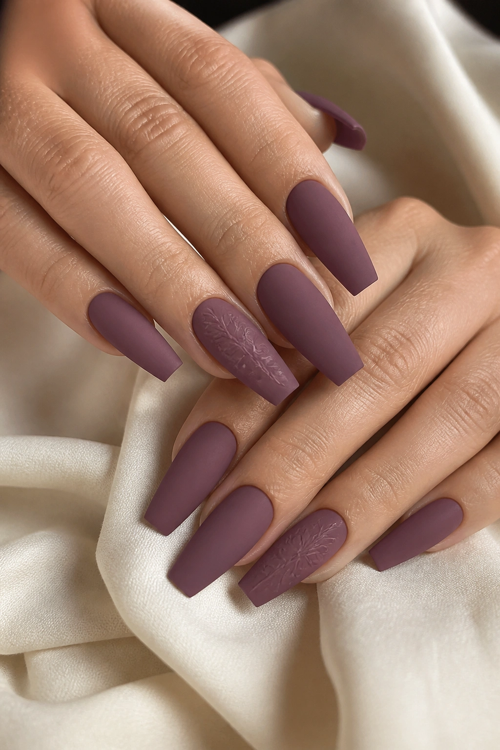 Close-up of plum matte coffin nails with tone-on-tone floral art
