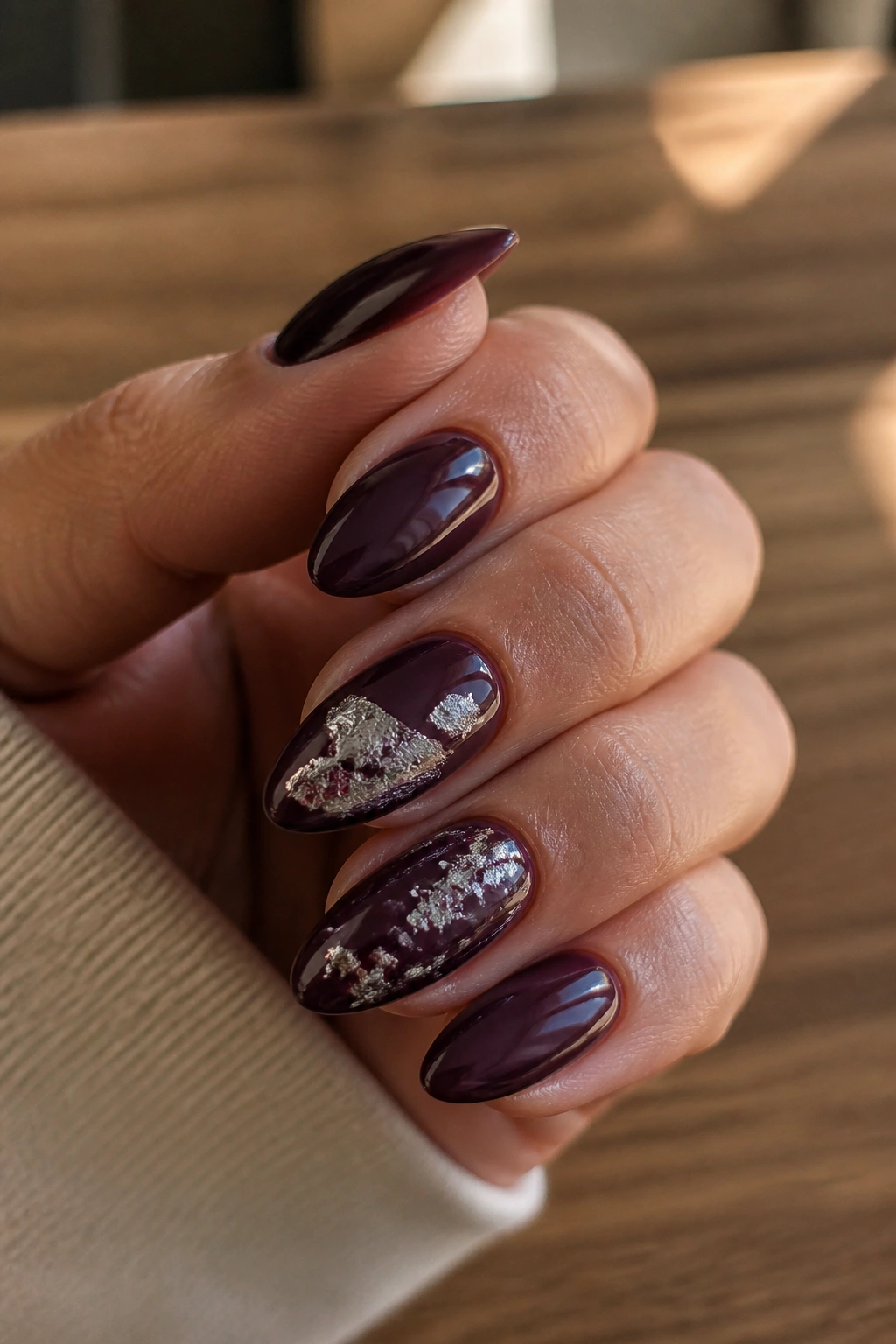 Close-up of almond nails in plum with irregular silver foil accents on a real hand