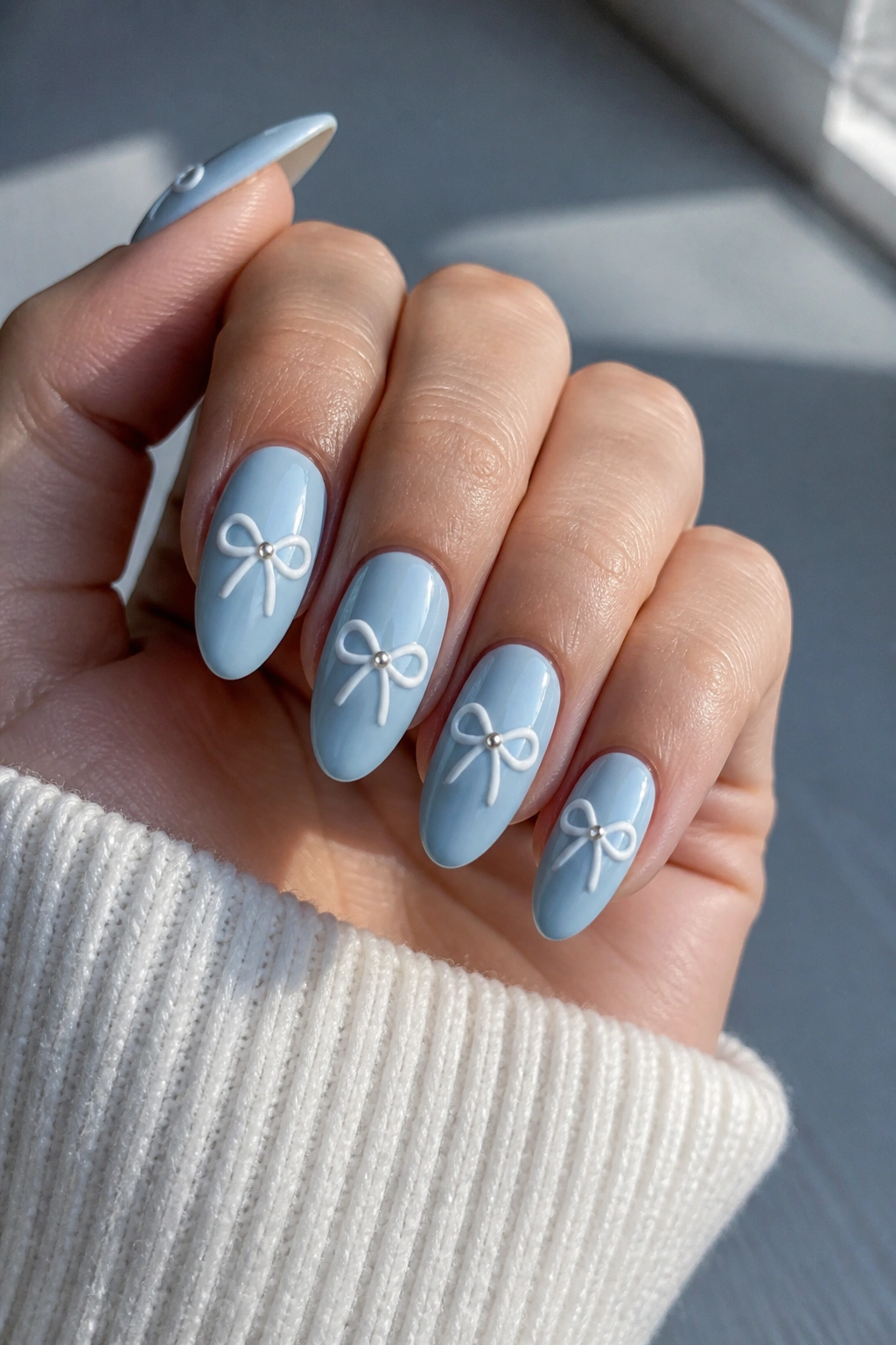 Close-up of porcelain blue almond nails with white bows