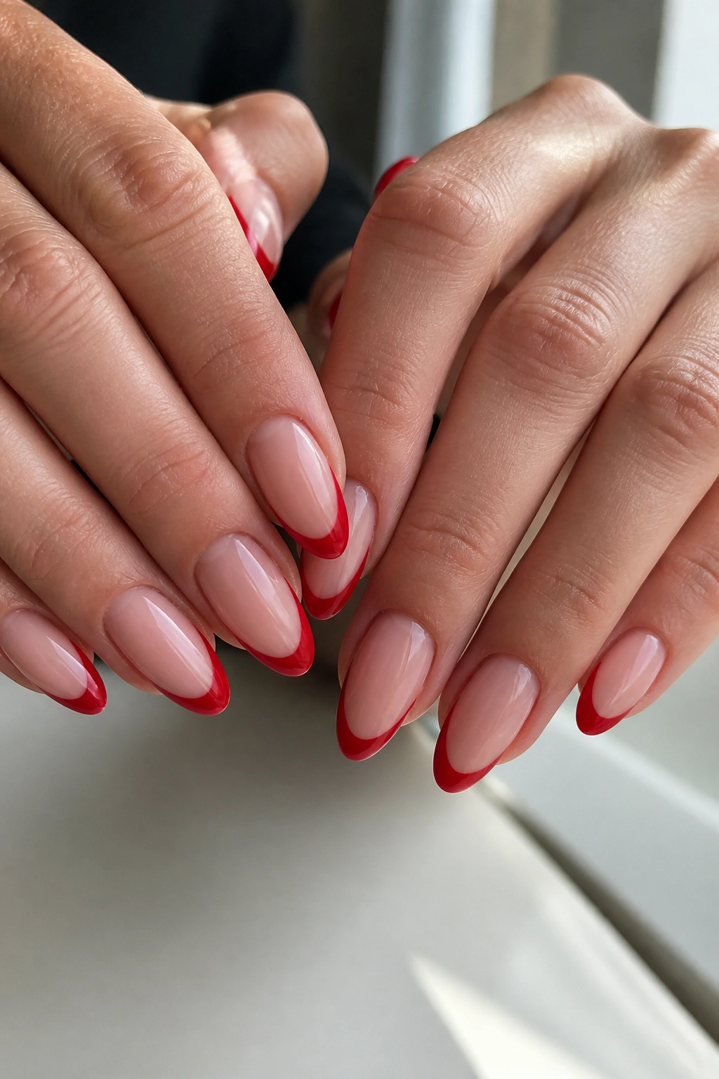 Close-up of almond nails with red French tips on a real hand