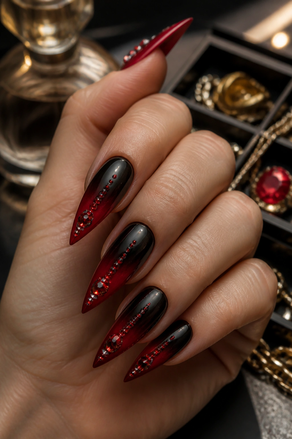 Hand with red jewel-accented ombre nails on a black fade.