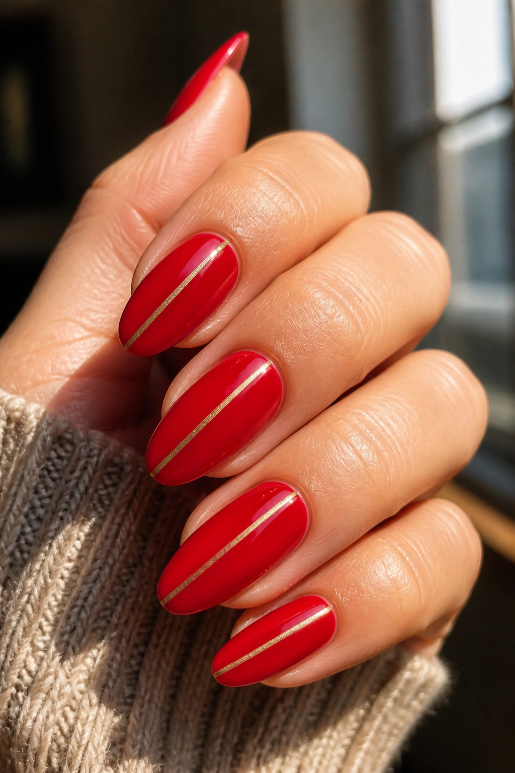 Close-up of nails with red polish and a thin gold stripe.