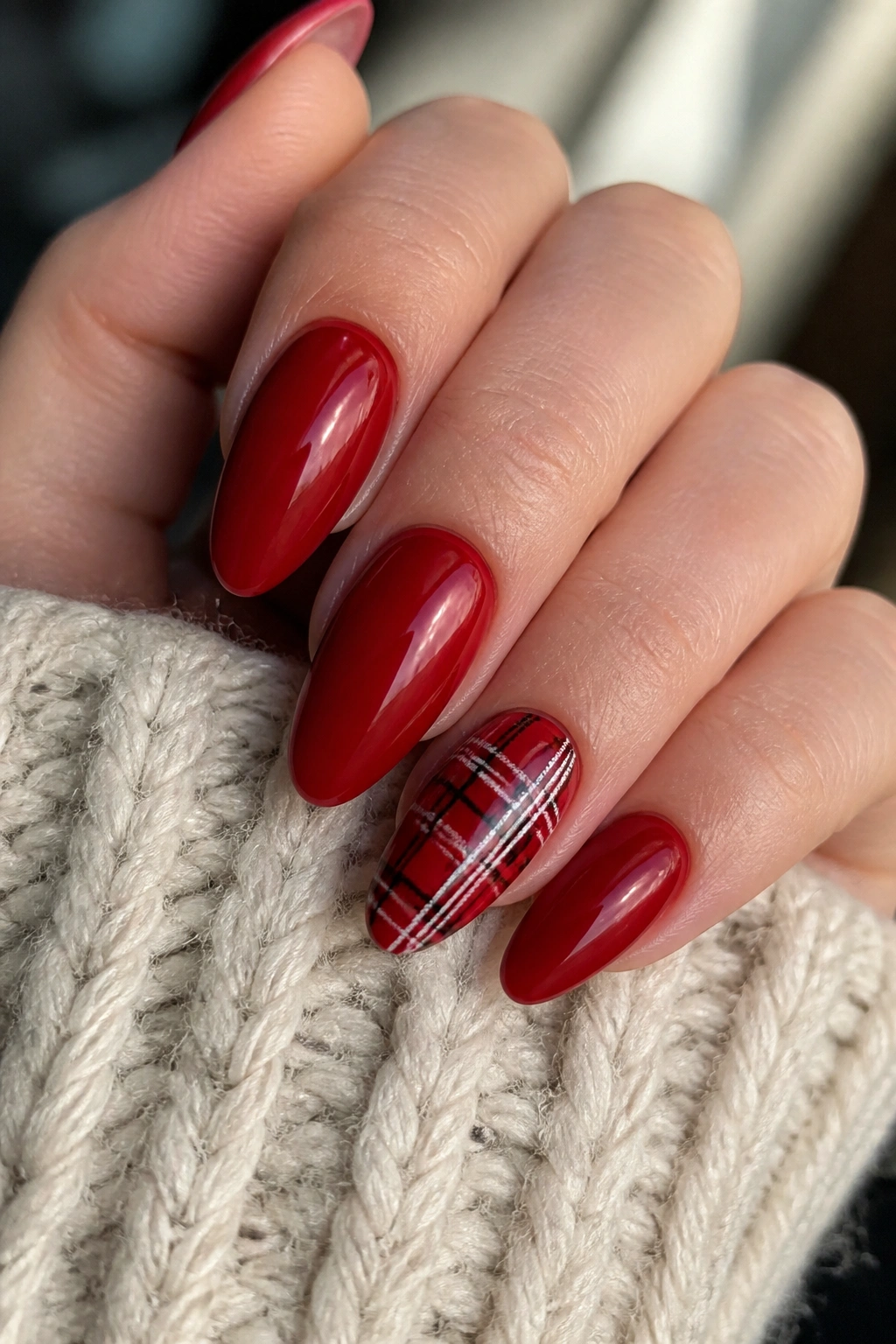 Close-up of real hand with red almond nails and a plaid accent nail