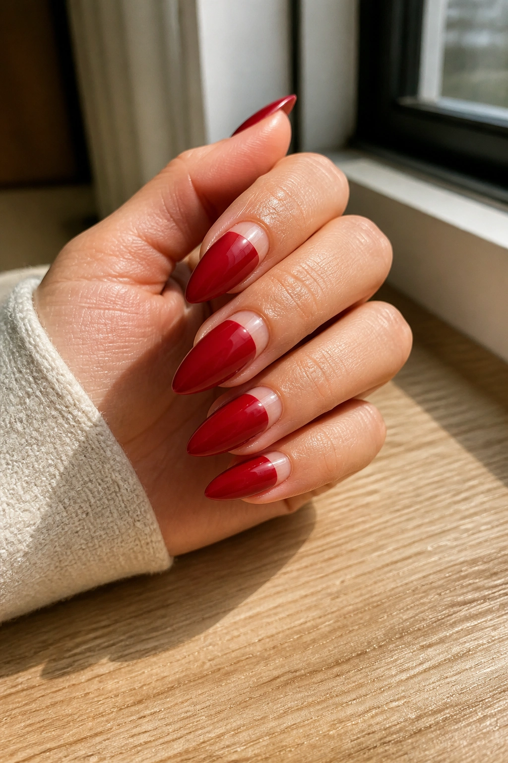 Close-up of a hand with reverse half-moon red almond nails.