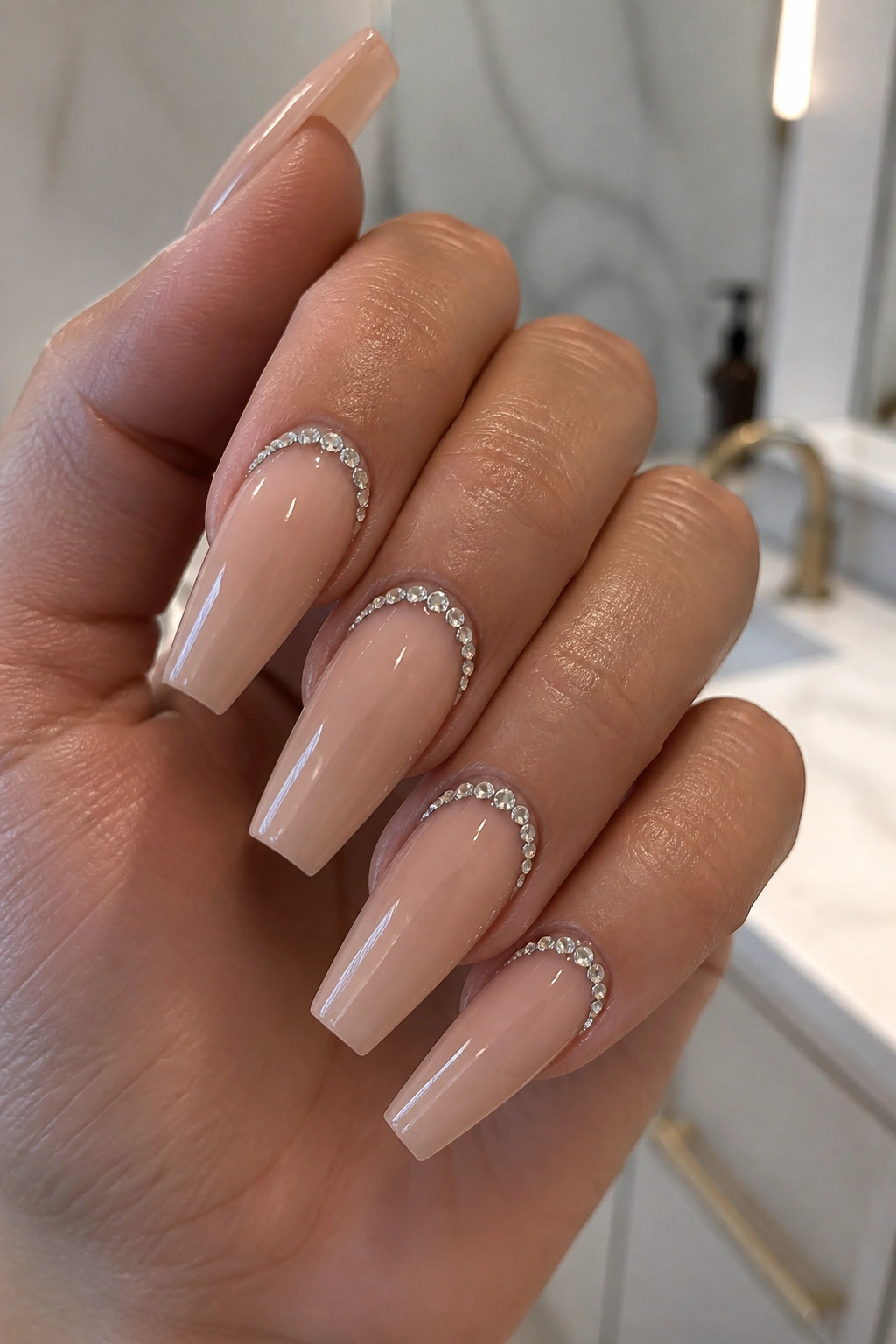 Close-up of rhinestone cuticle frames on glossy nude nails on a real hand