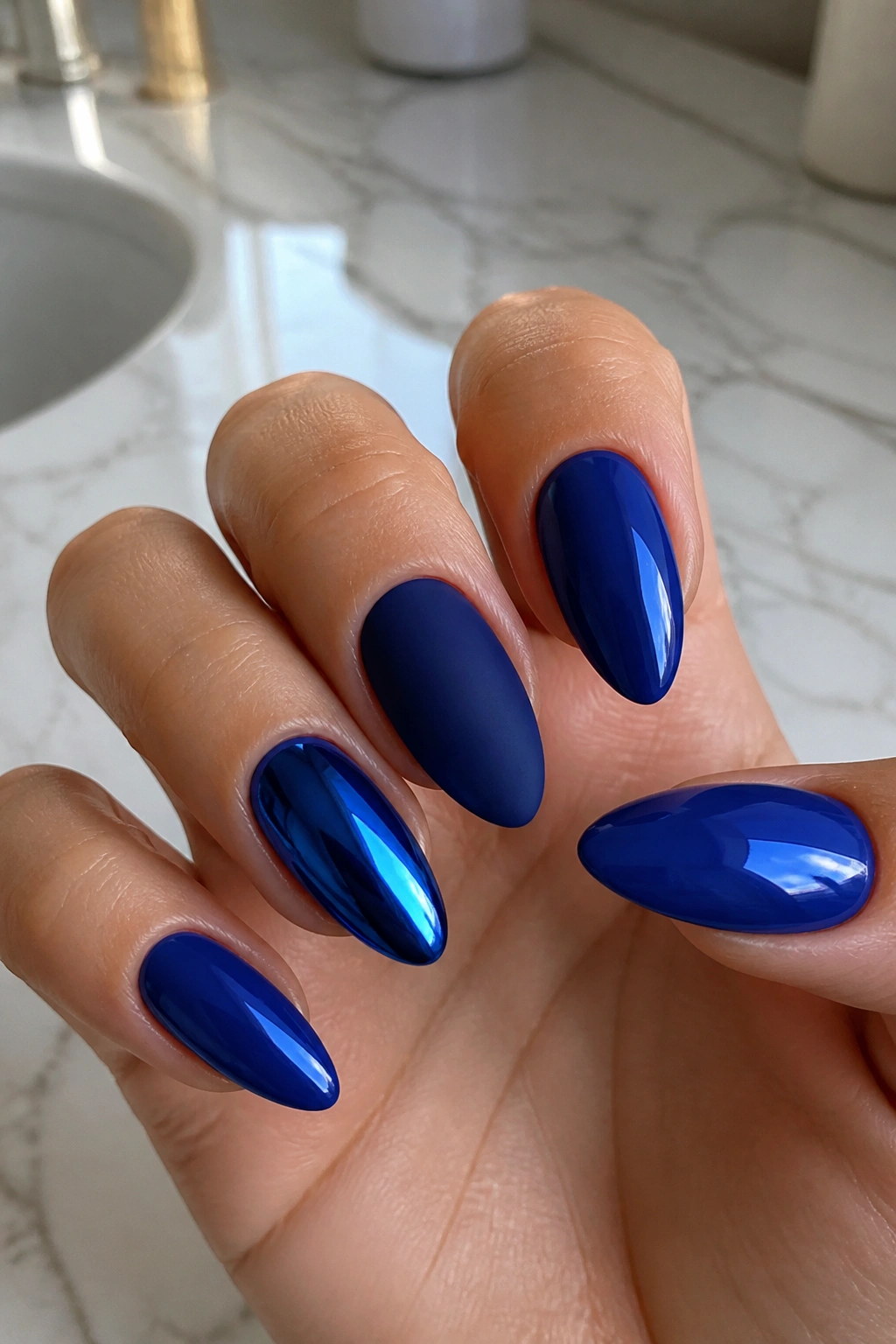 Close-up of royal blue almond nails with mixed finishes on a real hand