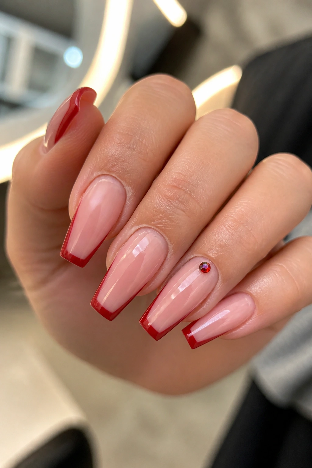Close-up of ruby micro-French coffin nails with a single crystal accent on the ring finger