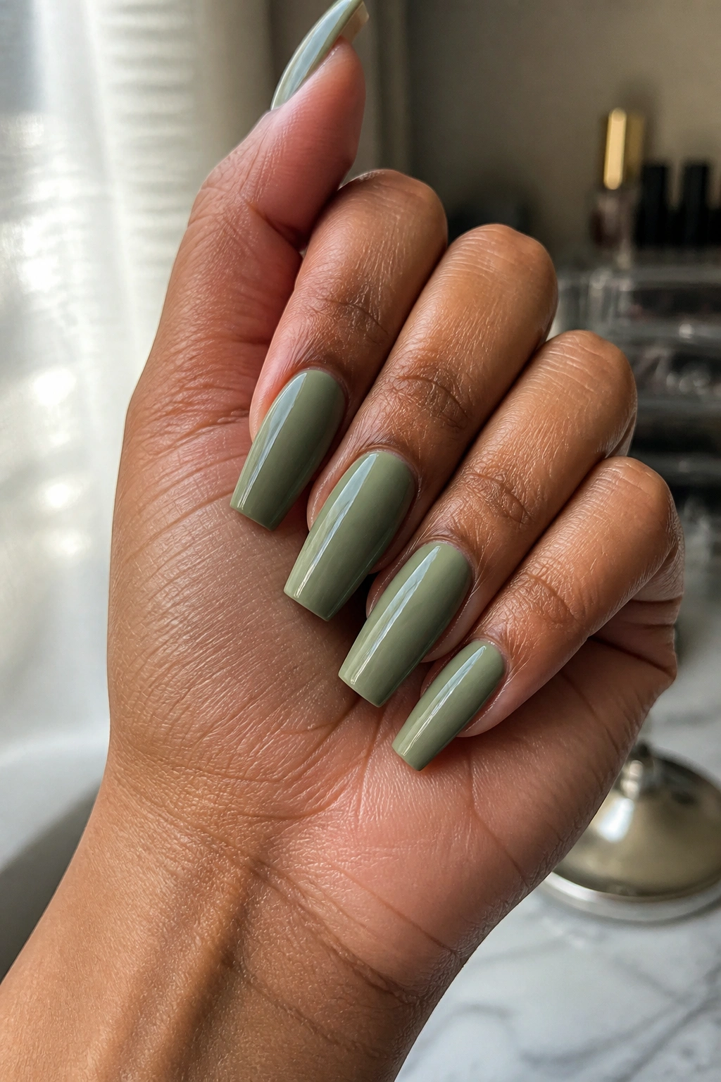 Close-up of warm-toned hand with sage green nails that flatter warm skin