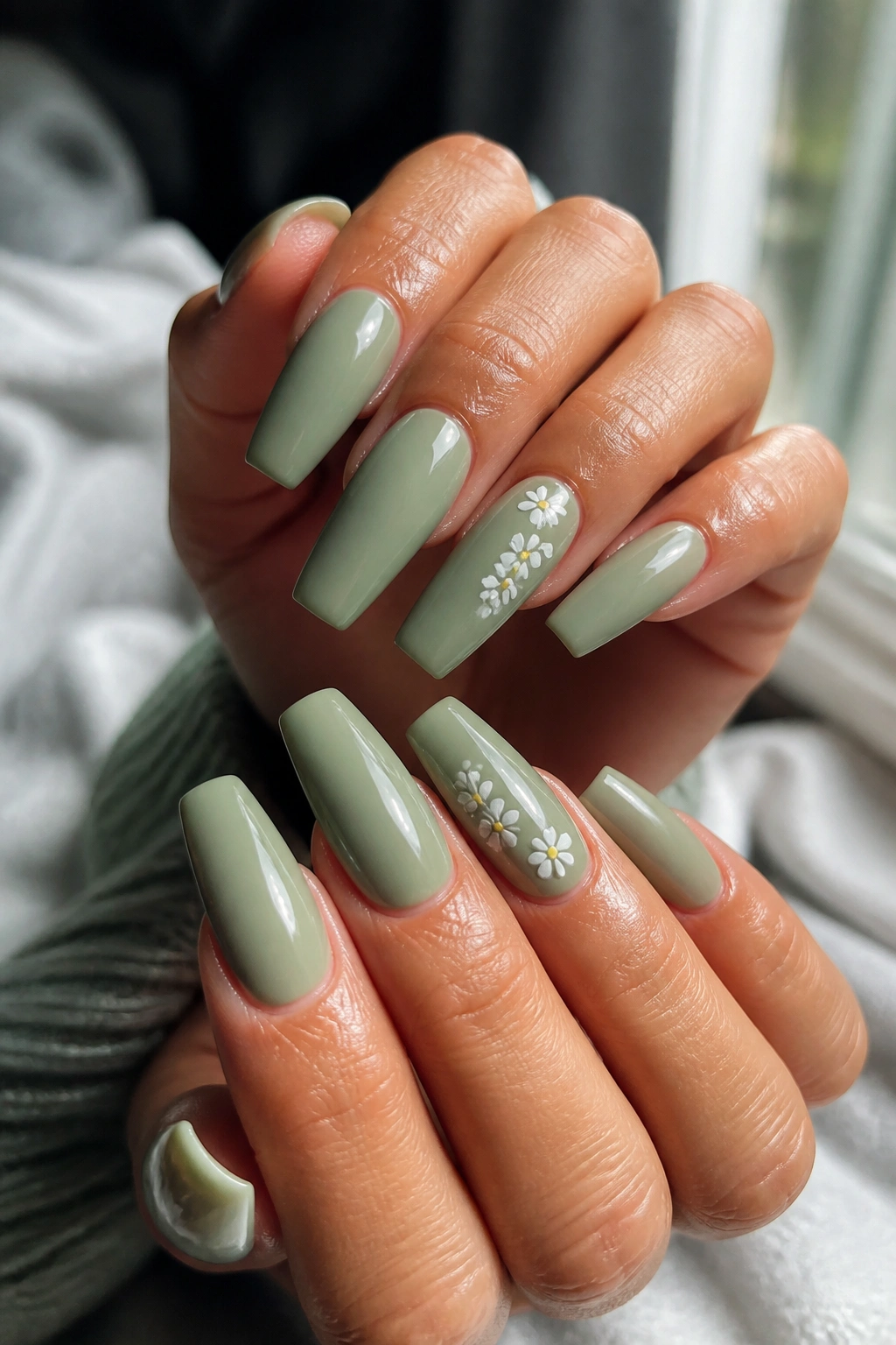 Close-up of sage green coffin nails with tiny white daisies on a real hand