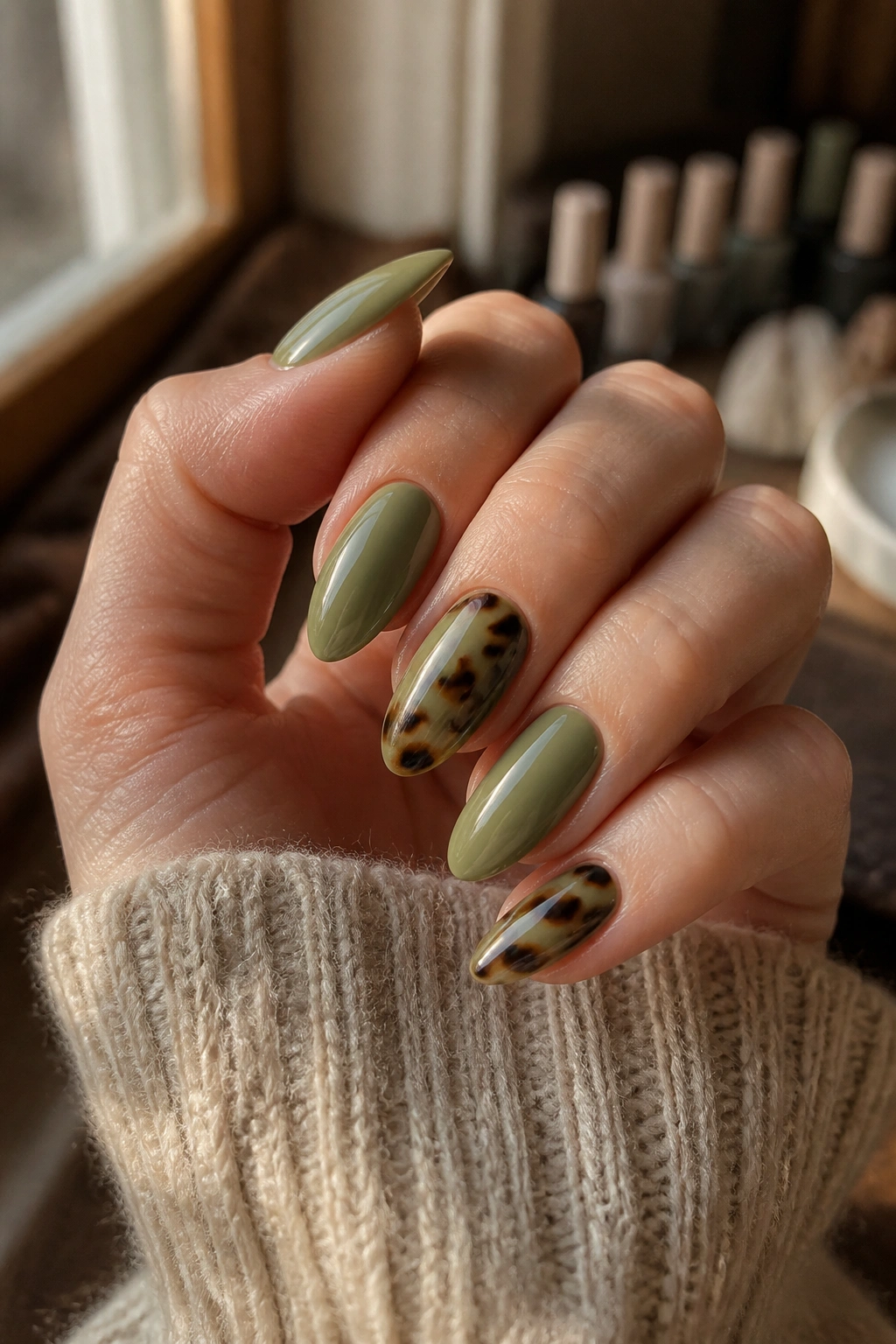 Close-up of sage green nails with tortoiseshell accent nails on almond fingers