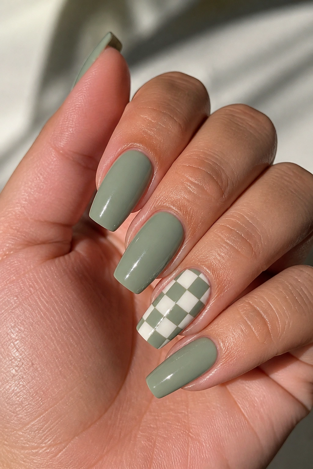Close-up of a hand with sage and ivory checkerboard accent nail