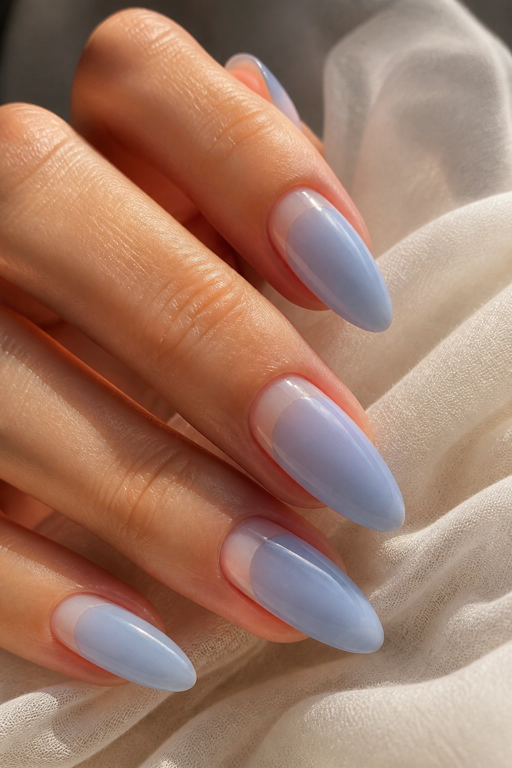 Close-up of almond nails with sheer sky blue polish over milky nude base.