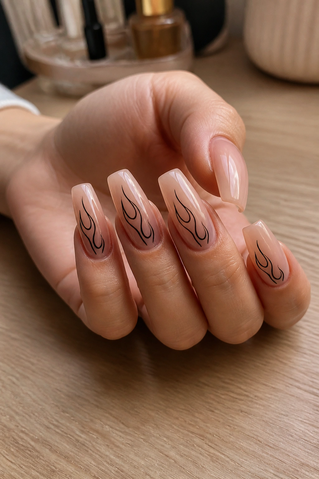 Close-up of sheer nude coffin nails with black flame art on a hand