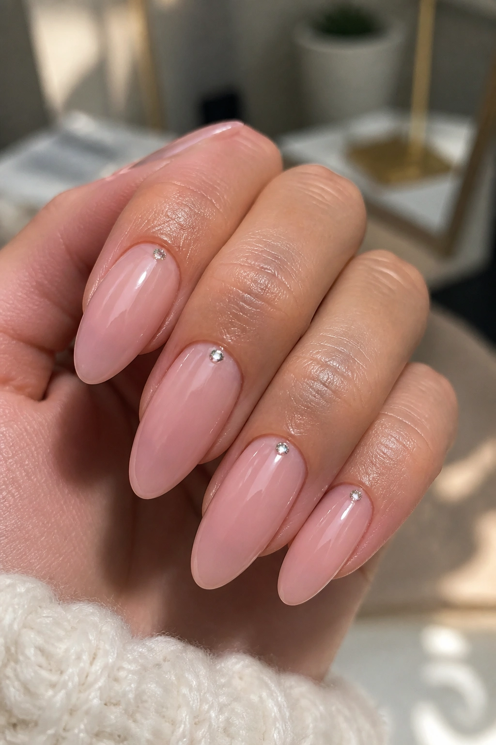 Close-up of sheer pink almond nails with tiny rhinestones near the cuticle.