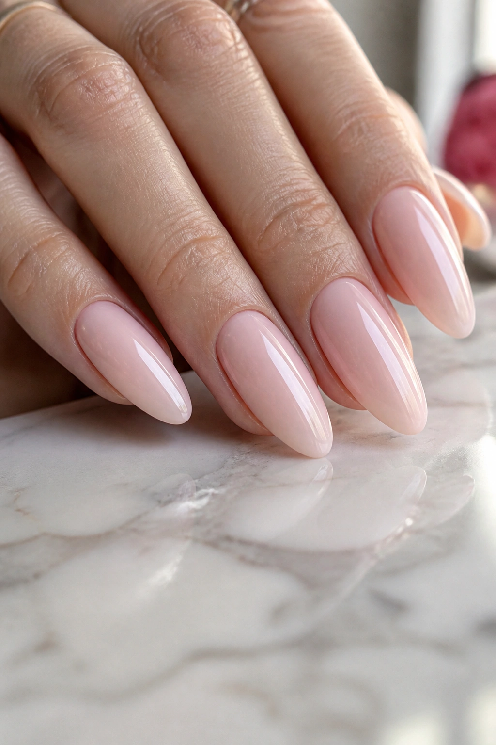 Close-up of a real hand with long almond nails in sheer ballet pink with high-gloss finish