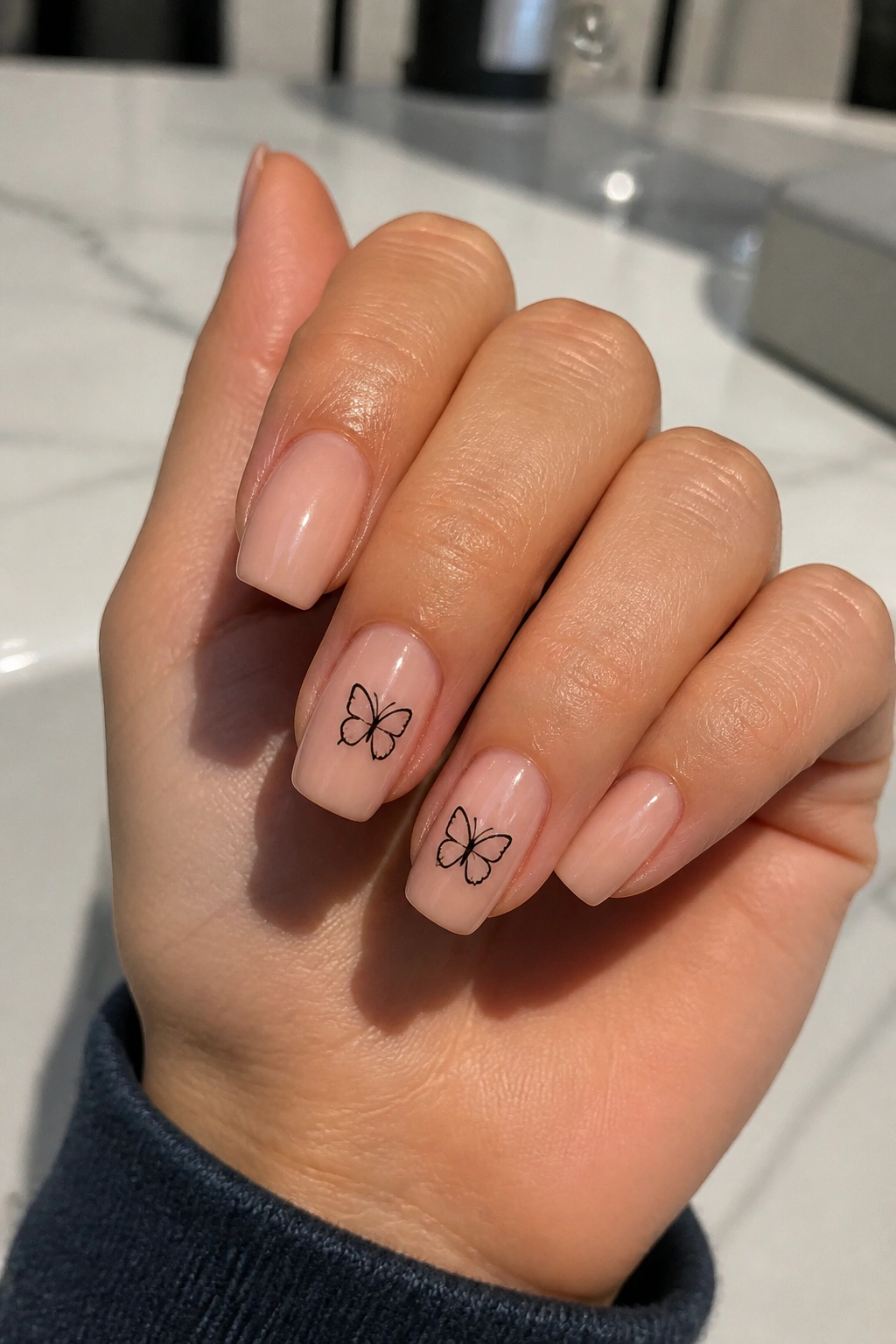 Close-up of shorter coffin nails with minimal butterfly outlines on a real hand