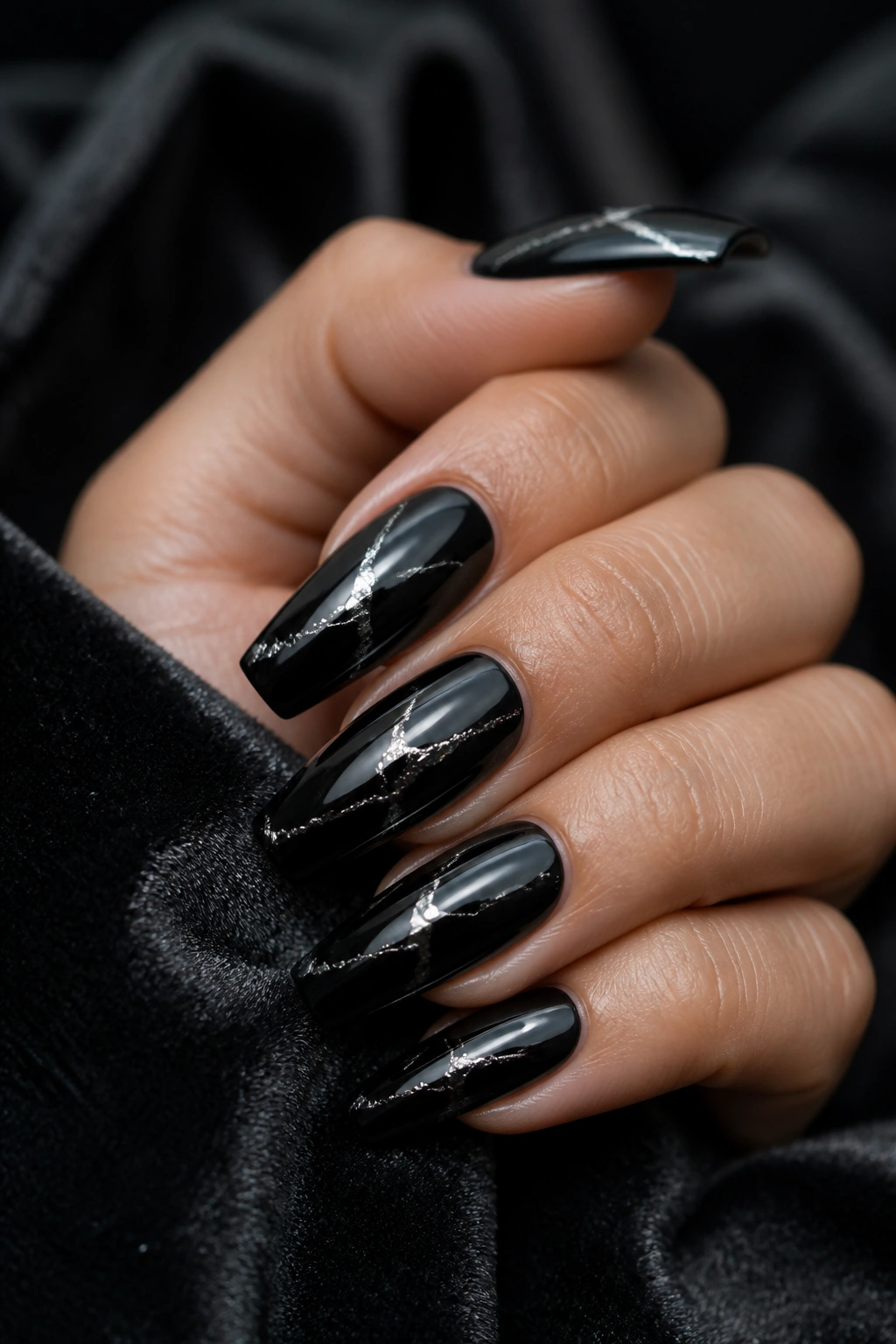 Close-up of black coffin nails with irregular silver foil cracks on a hand.